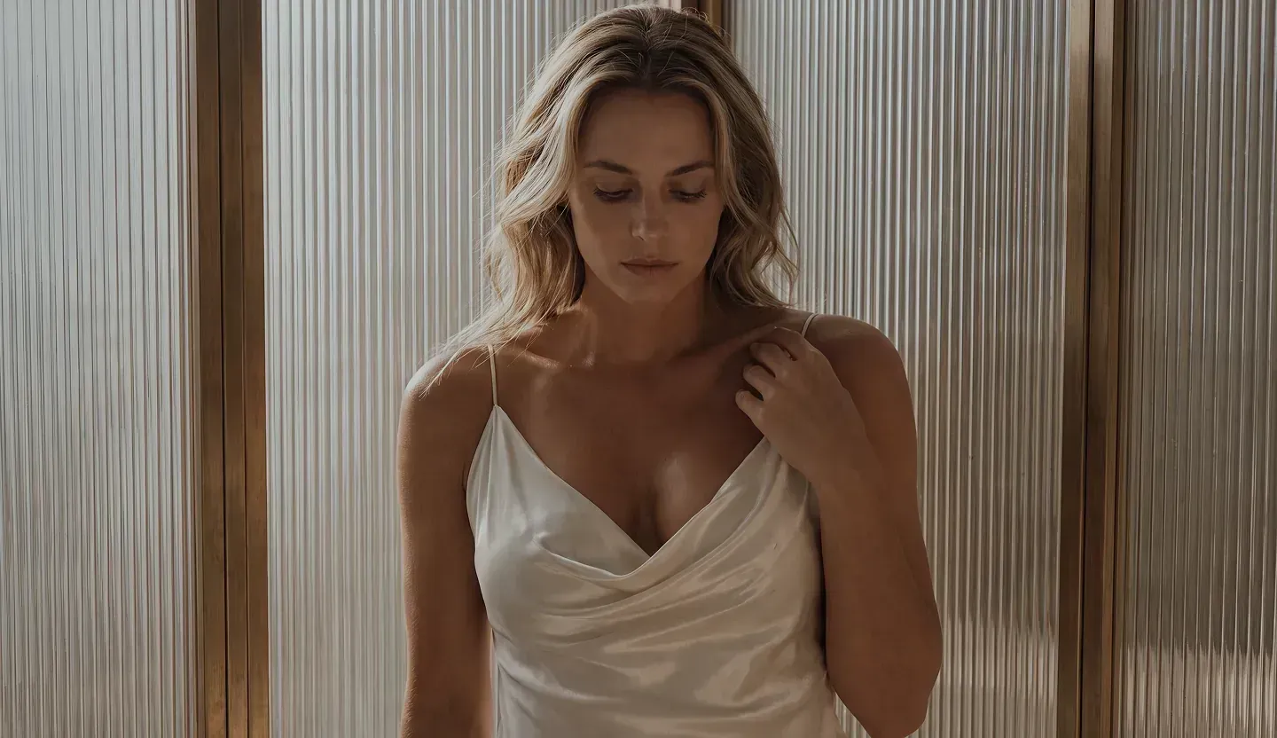 Woman tying a robe in a bright bedroom – breast surgery at Skulpturkliniken