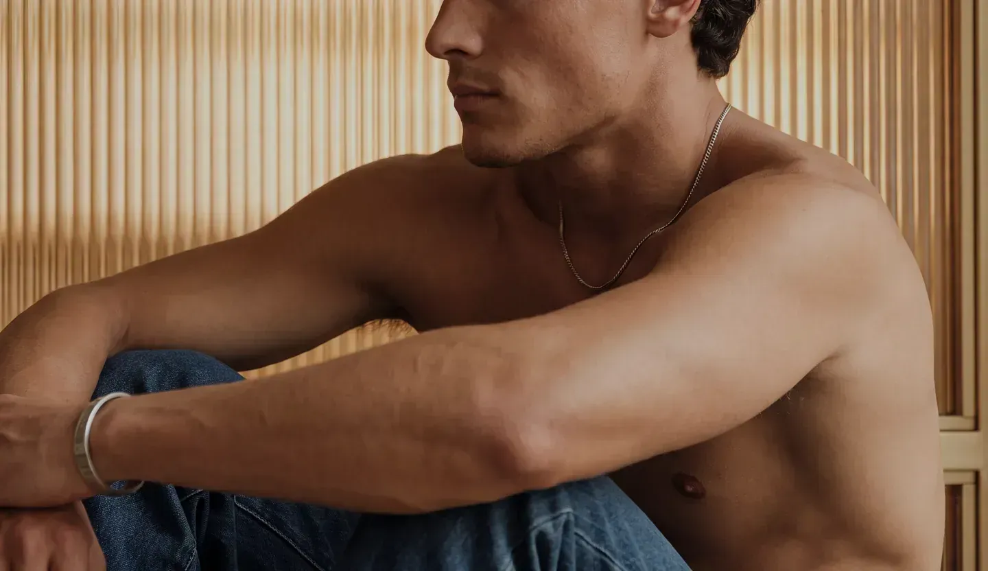Shirtless man with a towel over his shoulders in a bright changing room – male breast surgery at Skulpturkliniken