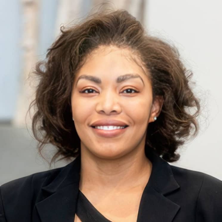 A woman with curly hair, wearing a black blazer, smiling at the camera.