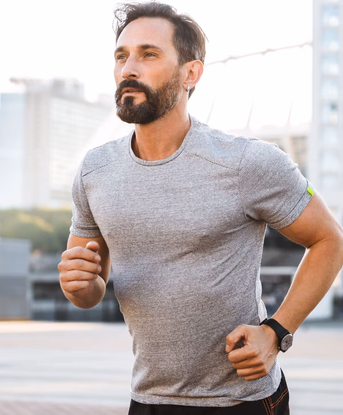 A man with a beard, wearing a gray athletic shirt, running with a focused expression on his face.
