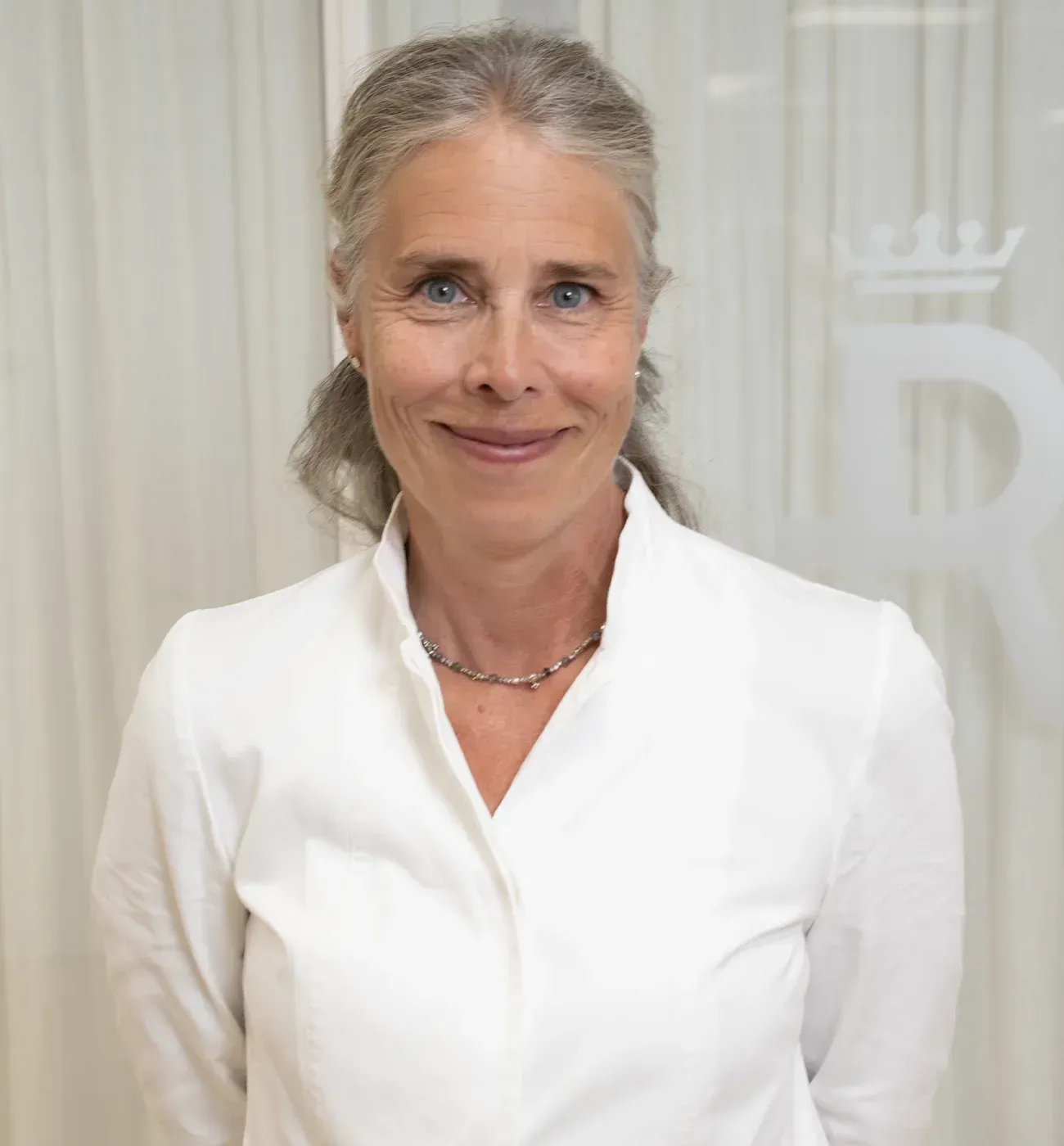 Dr. Stina Klasson in a white clinical jacket, standing in a Reformkliniken consulting room.