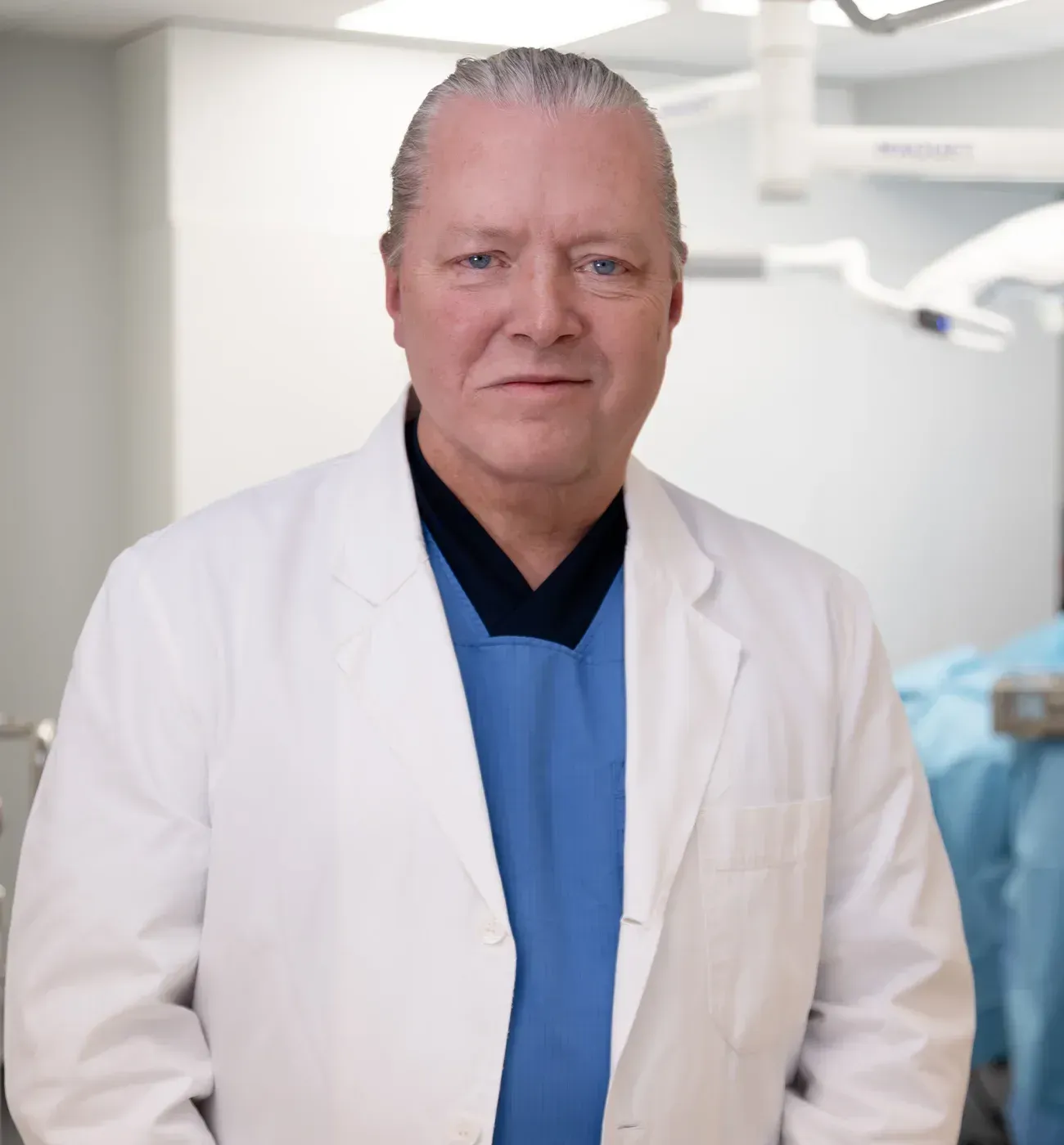 Dr. Tuve Mårtensson in a white medical coat over blue scrubs, standing in an operating room.
