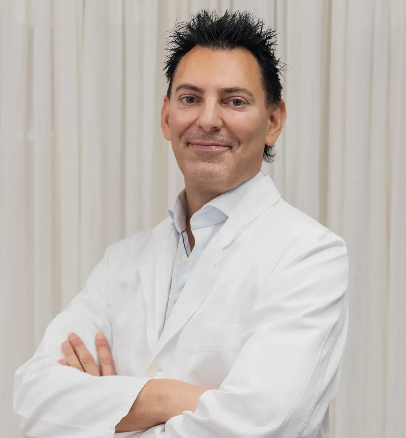 Dr. Zvonko Cogelja in a white medical coat, arms crossed, standing in a clinic room.