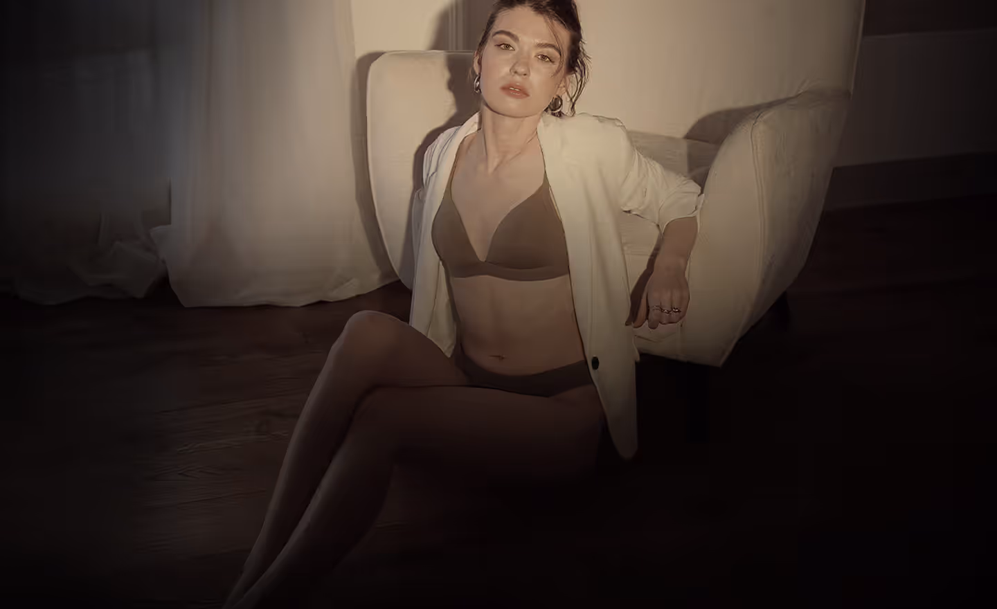 A seated woman wearing a brown bikini and a white blazer, with her hair pulled back.