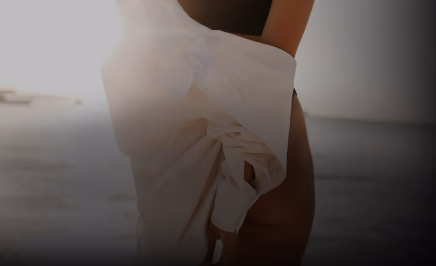 A person holding a white shirt while standing in shallow water, with bright sunlight illuminating the scene.