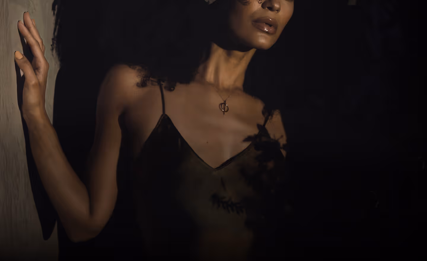 A woman with curly hair wearing a simple necklace featuring a circular pendant, with her shoulders partially visible.