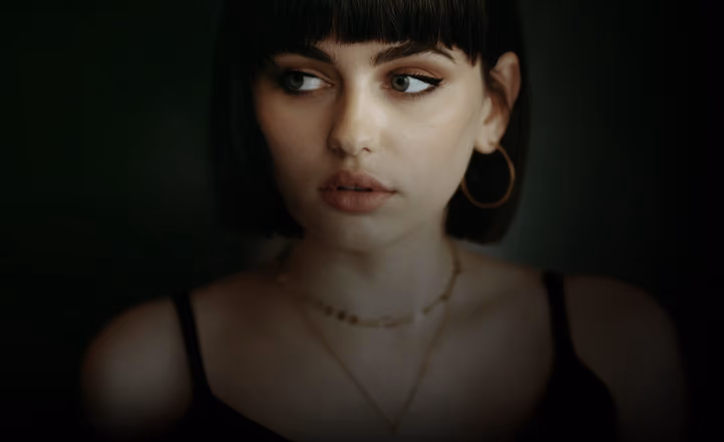 A close-up portrait of a young woman with straight dark hair and bangs, wearing hoop earrings and delicate necklaces, looking off to the side with a neutral expression.