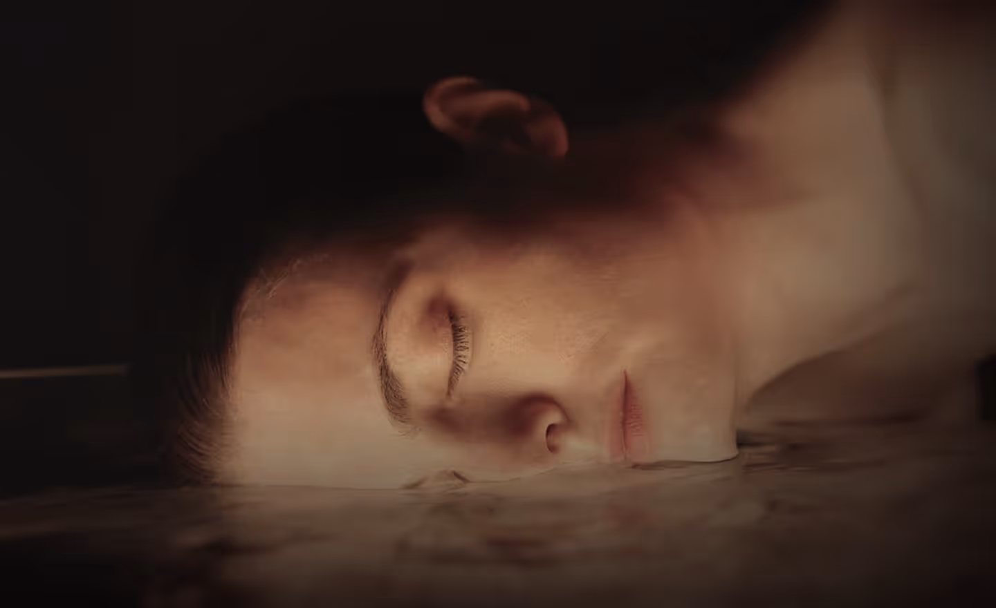A close-up image of a woman lying on a smooth surface with her face turned to the side, eyes closed and expression serene.