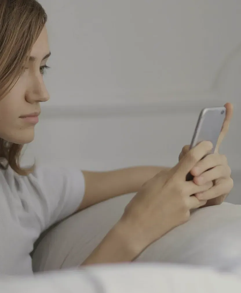 Person som tittar på mobiltelefon i sängen med neutral bakgrund
