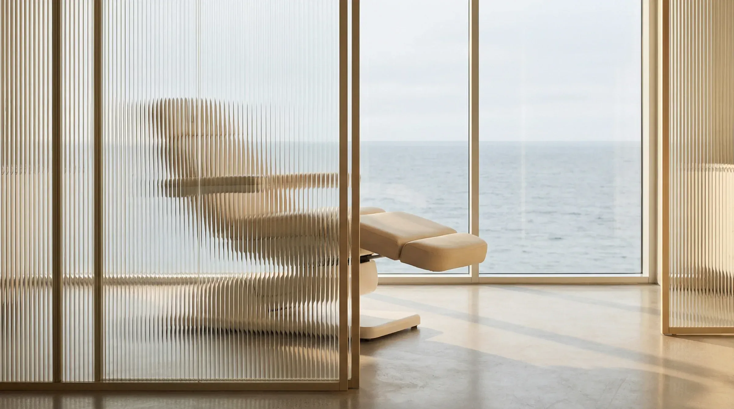 Skulpturkliniken treatment room with a reclining chair and a sea view through floor-to-ceiling windows.